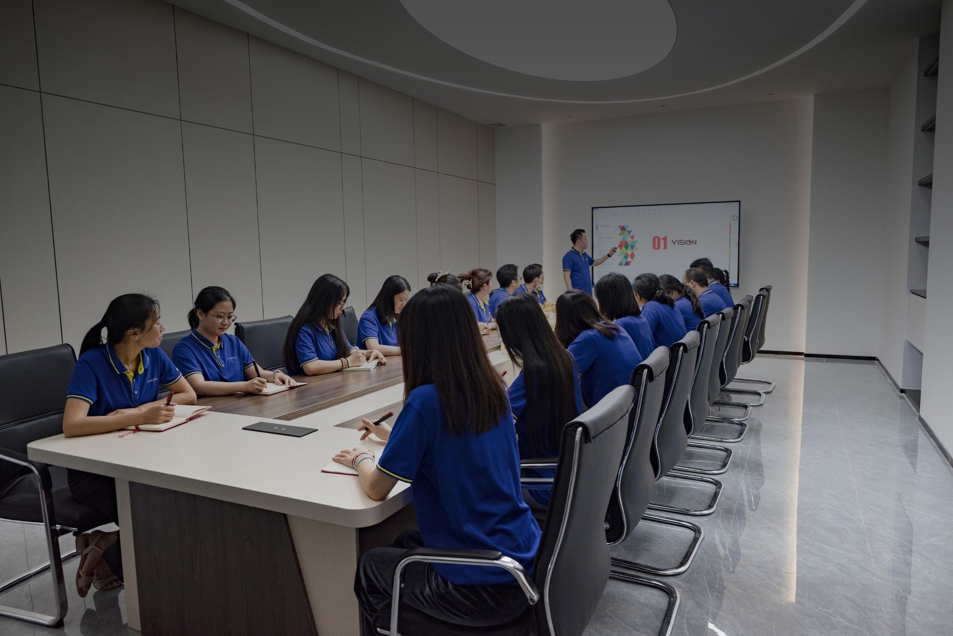 Group of people in blue shirts attending a presentation in a conference room.