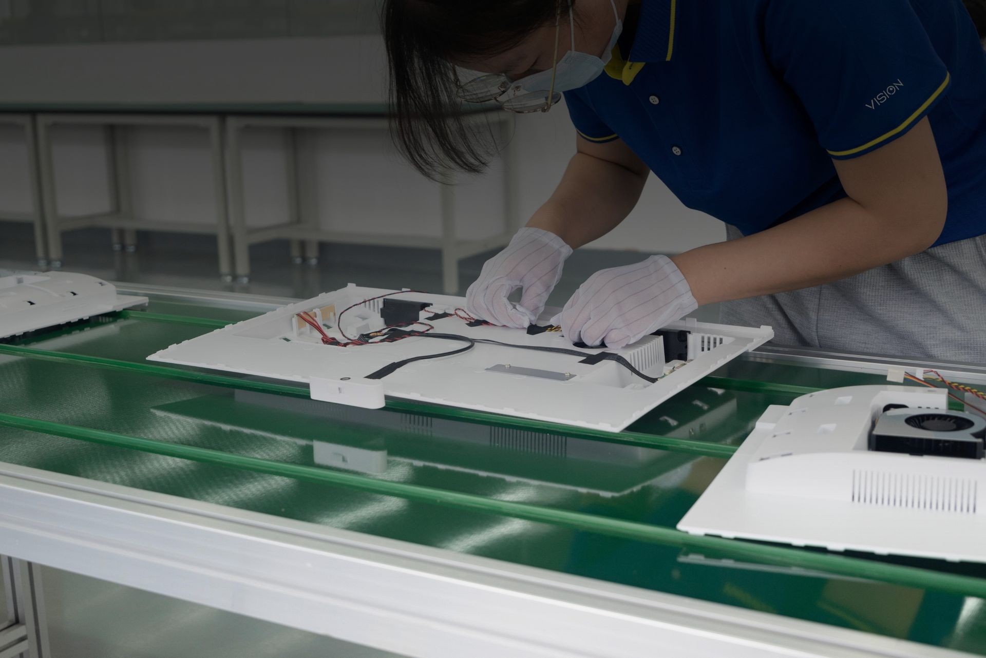 Technician assembling electronic components on a white panel in a clean room environment.